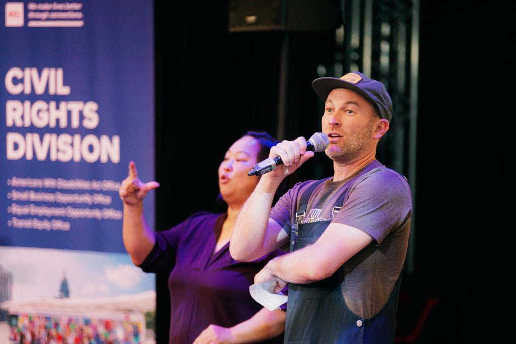man speaking into microphone wearing overalls